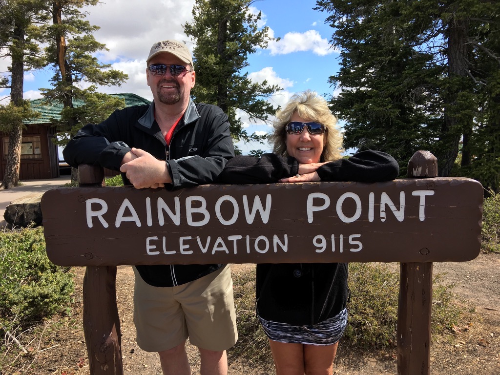 Joby Horn and his wife smiling behind the Rainbow Point sign