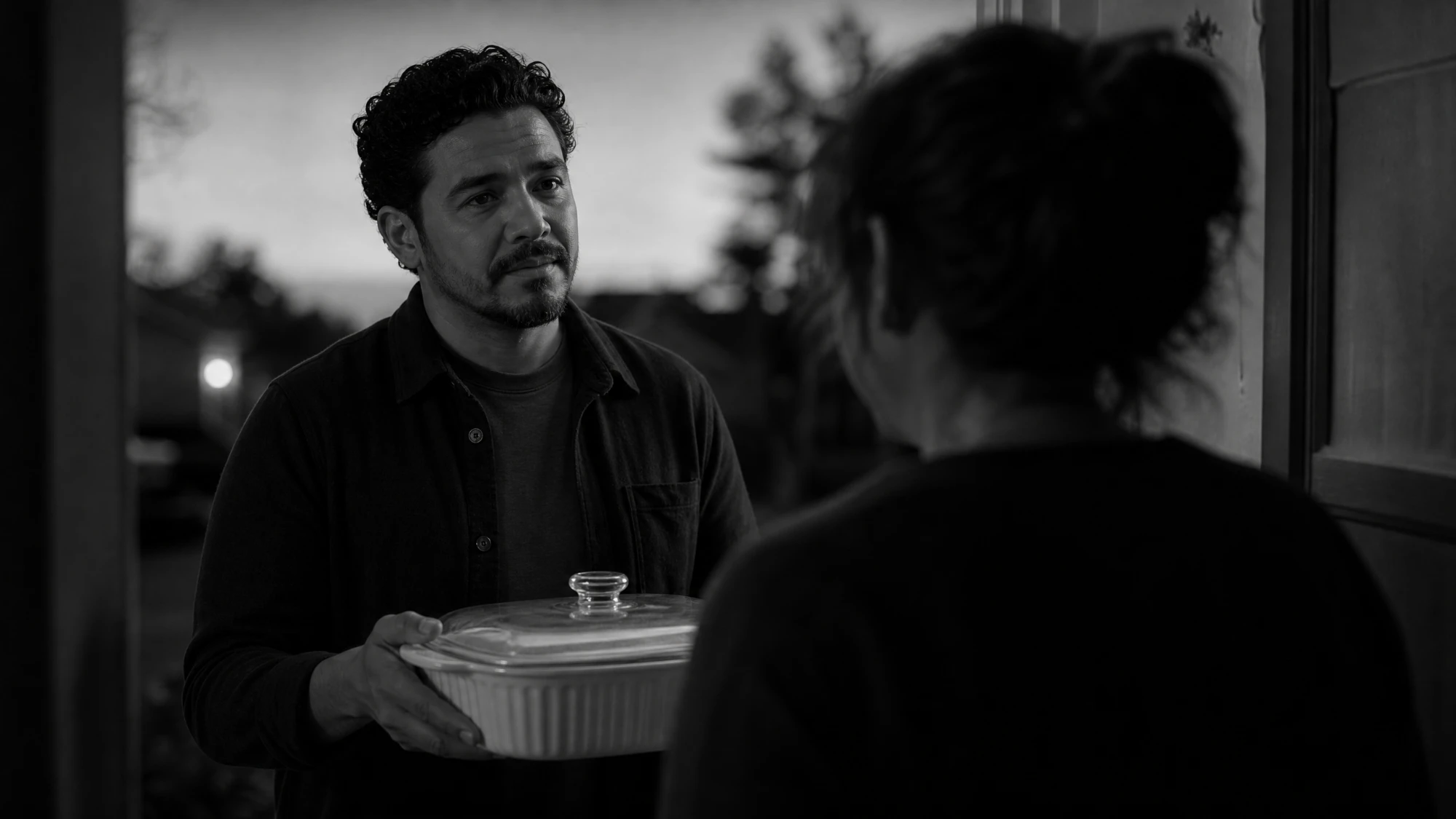 A friend arriving at a doorway with a covered dish for someone grieving, in black and white
